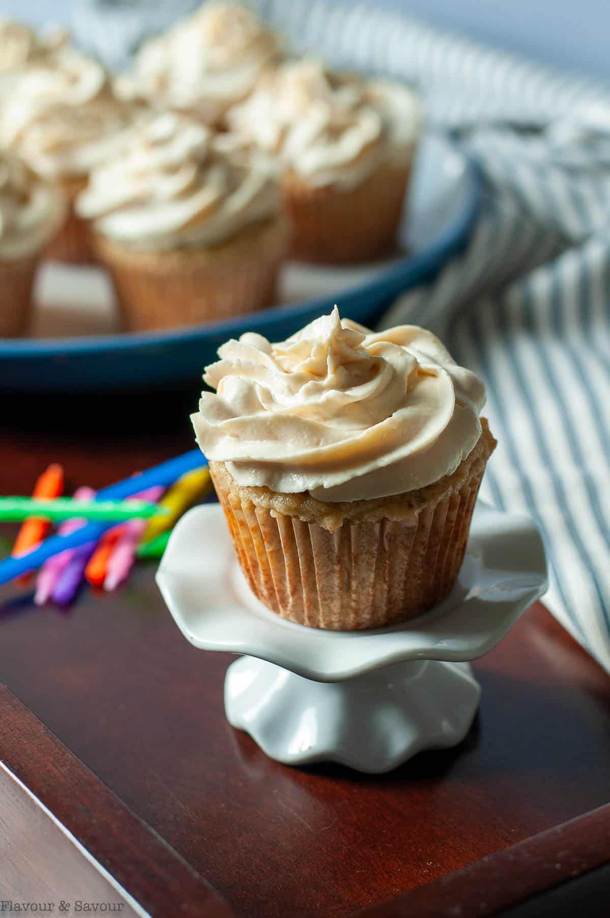 A banana cupcake with cream cheese frosting on a cupcake stand.