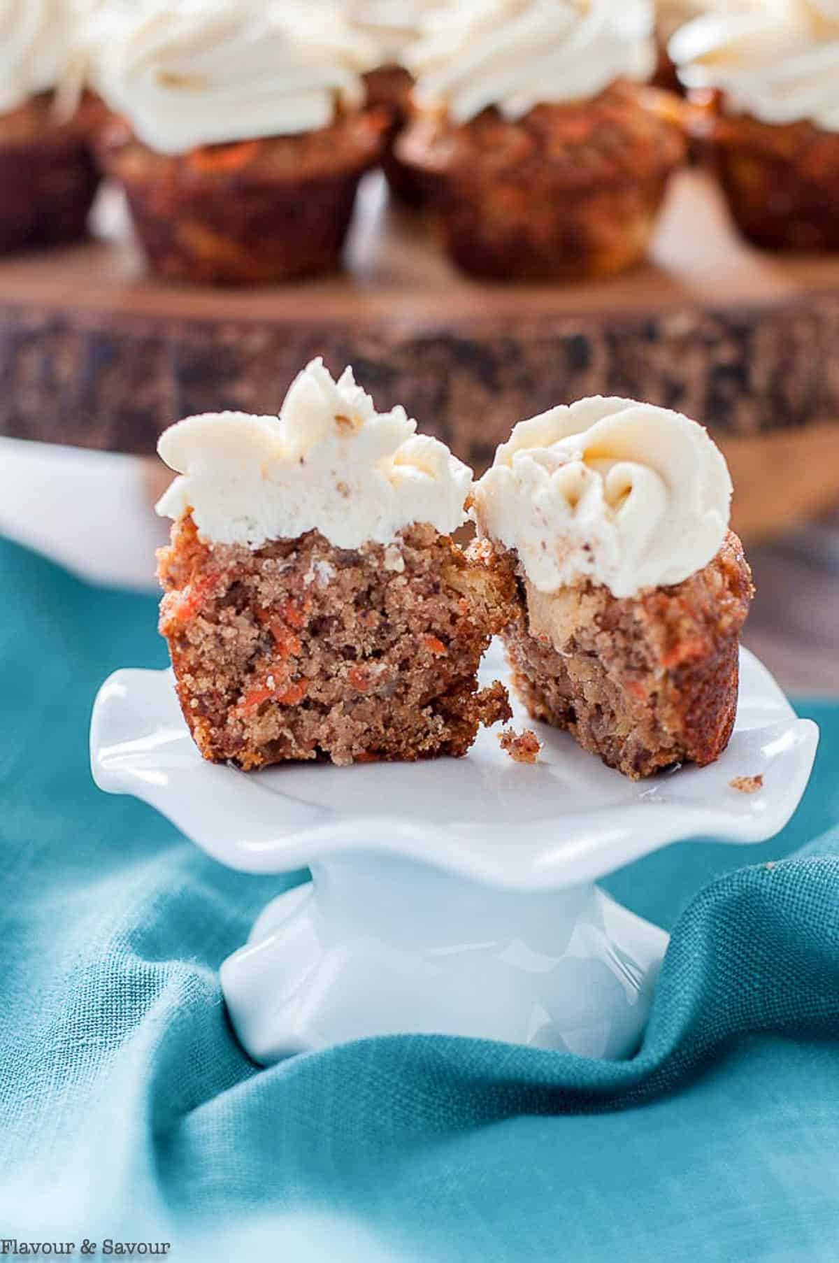 A frosted carrot cake cupcake split in half to show the inside.