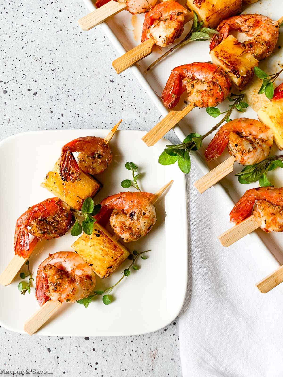 A platter of grilled shrimp or prawn kabobs with pineapple and a small plate with two skewers.