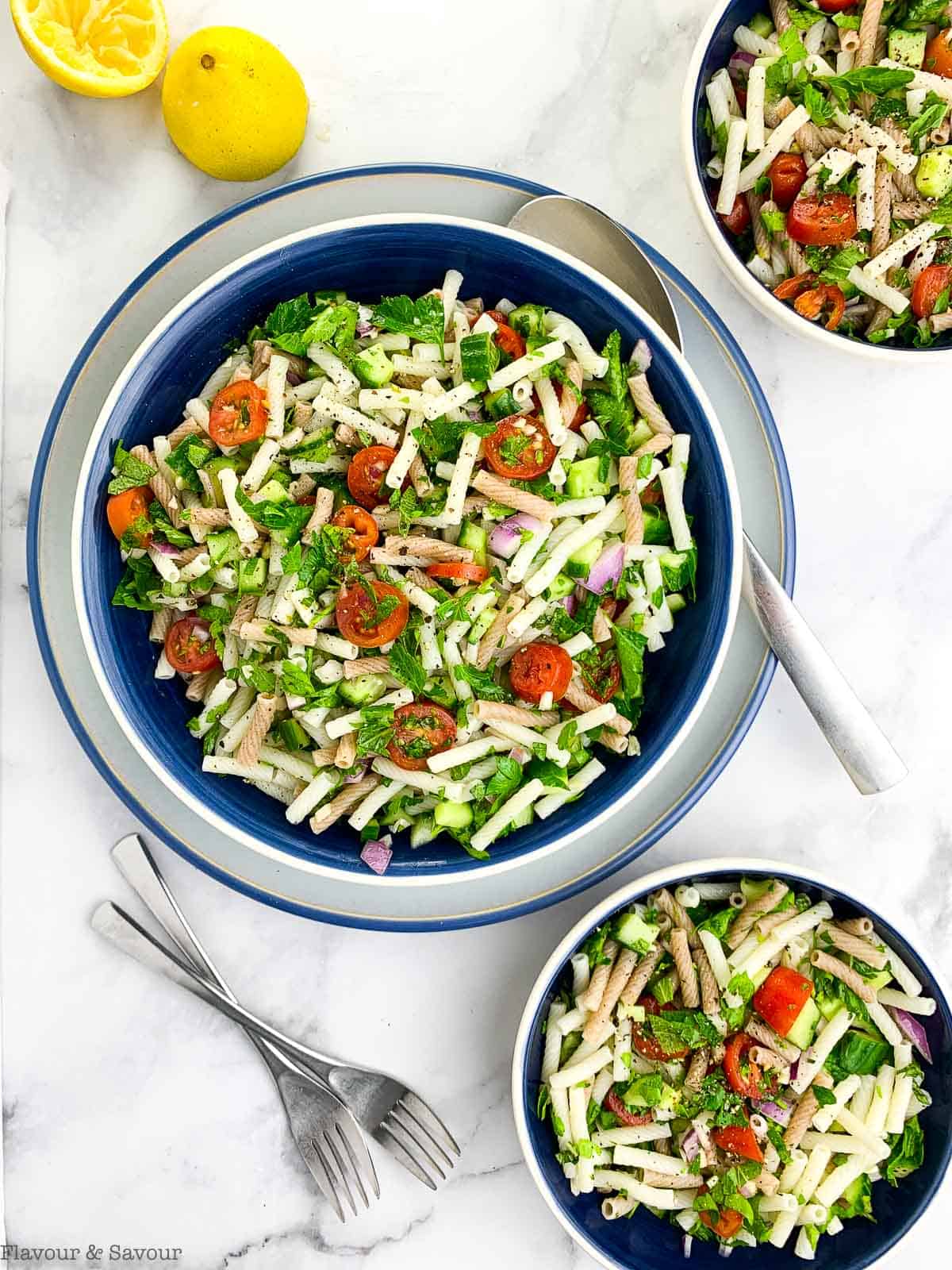 Overhead view of a serving bowl and two side dishes of tabouli pasta salad.