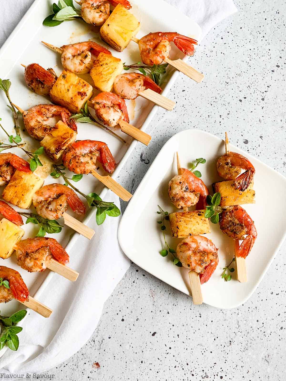 A platter of grilled shrimp or prawn kabobs with pineapple and a small plate with two skewers.