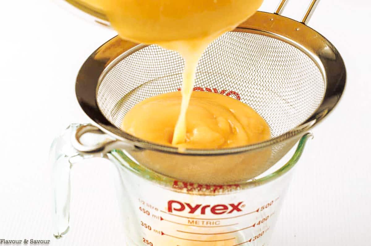 Straining lemon curd through a sieve into a measuring cup