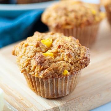Two gluten-free mango muffins with mango chunks and coconut on a board.
