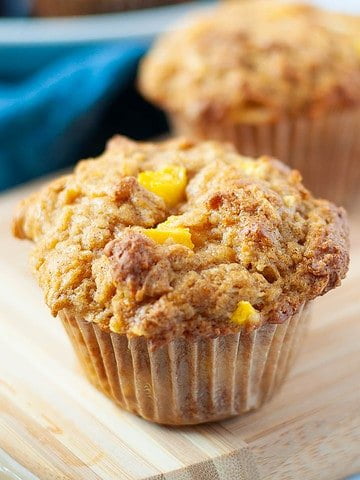 Two gluten-free mango muffins with mango chunks and coconut on a board.