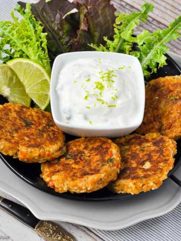 four salmon patties on a plate with a small bowl of lime sauce and lime wedges