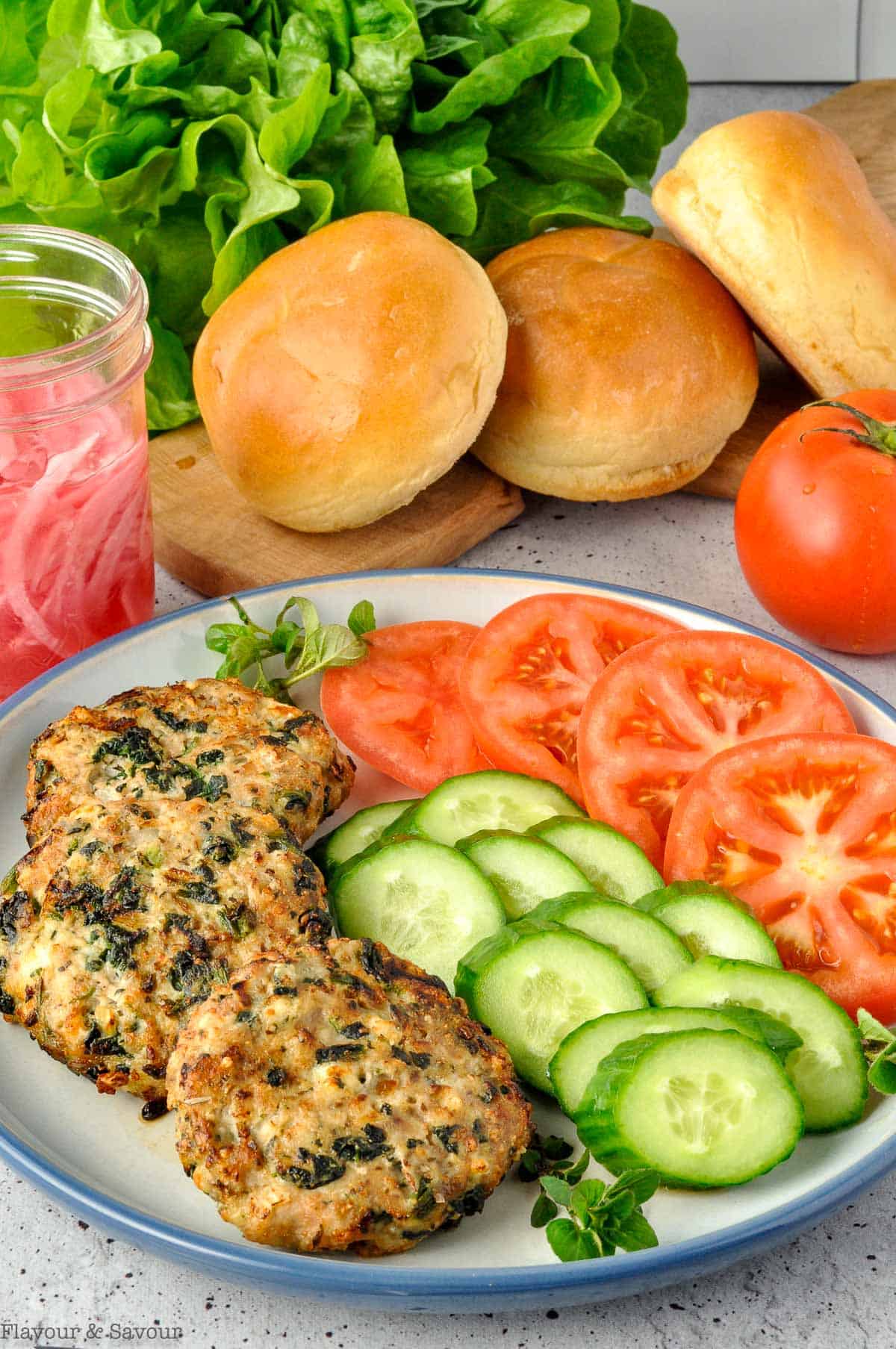 Ingredients for Greek Chicken Burgers arranged on a plate with buns and lettuce.