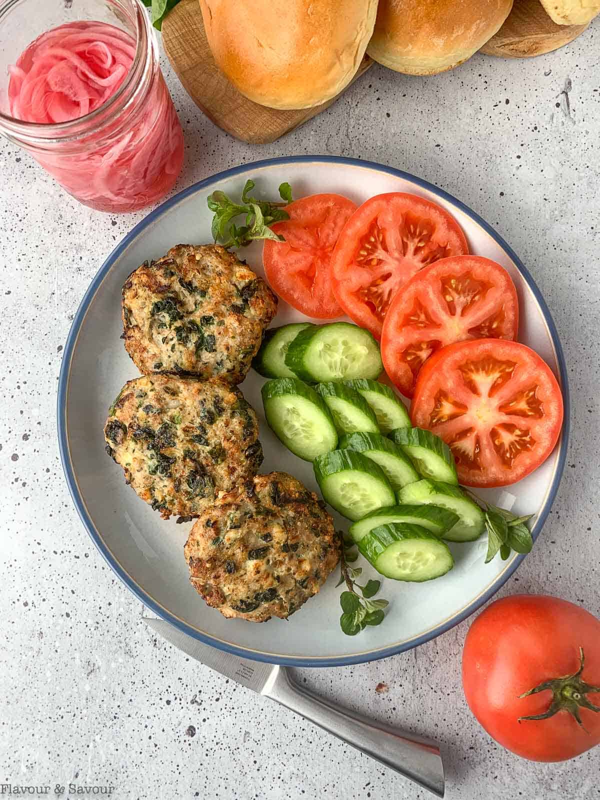 Air Fried Greek Chicken Burgers on a palte with sliced tomatoes and cucumbers