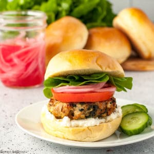 Greek Chicken Burger with spinach and feta on a brioche bun with lemon-garlic feta spread, sliced tomato, pickled red onions and lettuce leaves.