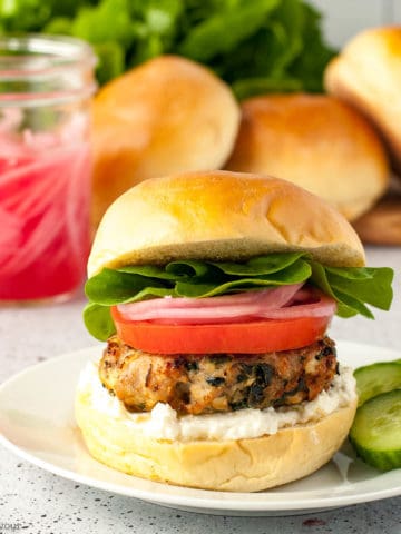 Greek Chicken Burger with spinach and feta on a brioche bun with lemon-garlic feta spread, sliced tomato, pickled red onions and lettuce leaves.