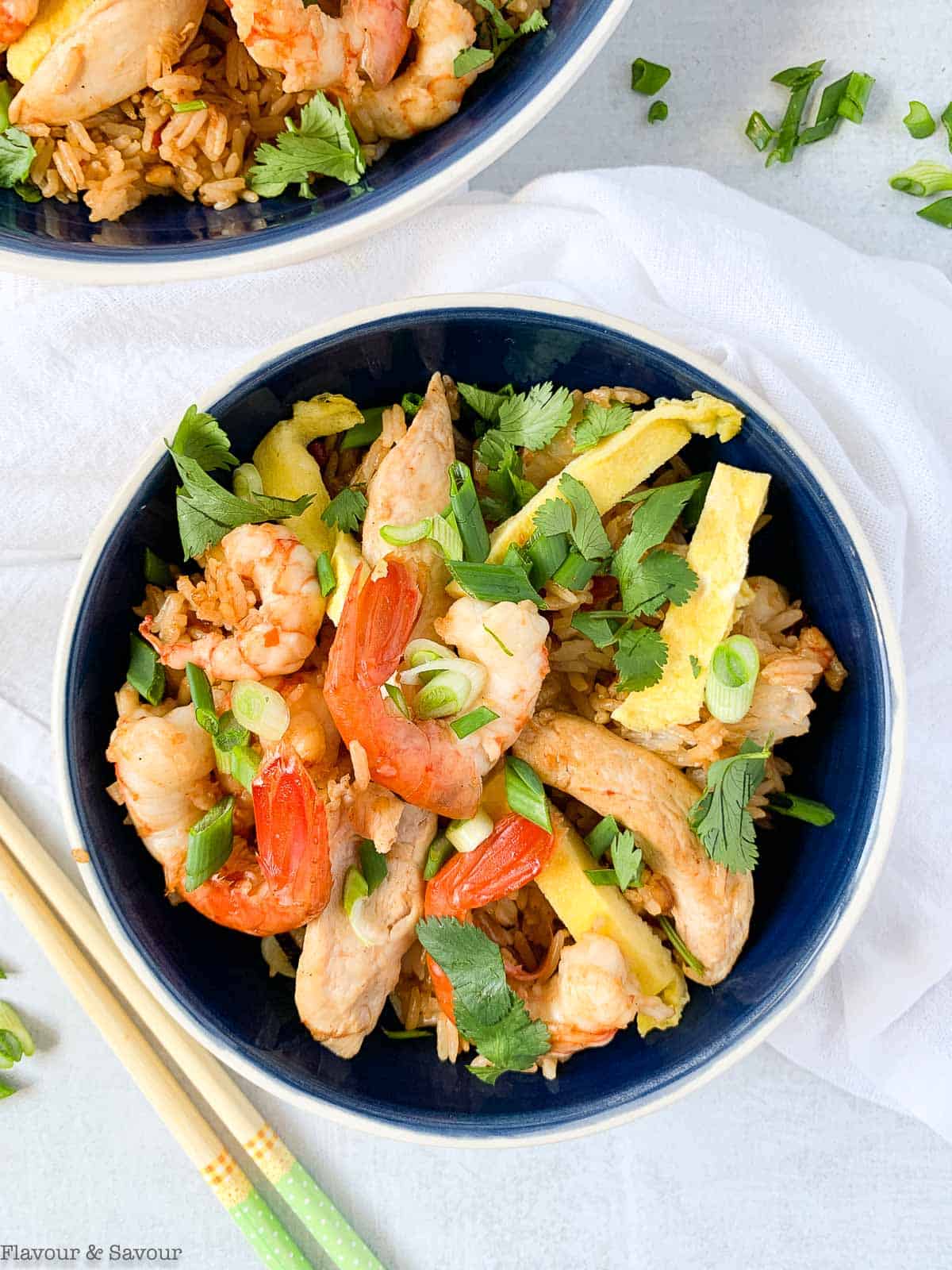 Overhead view of a bowl of Nasi Goreng, fried rice with chicken strips, shrimp, green onions and cilantro leaves.