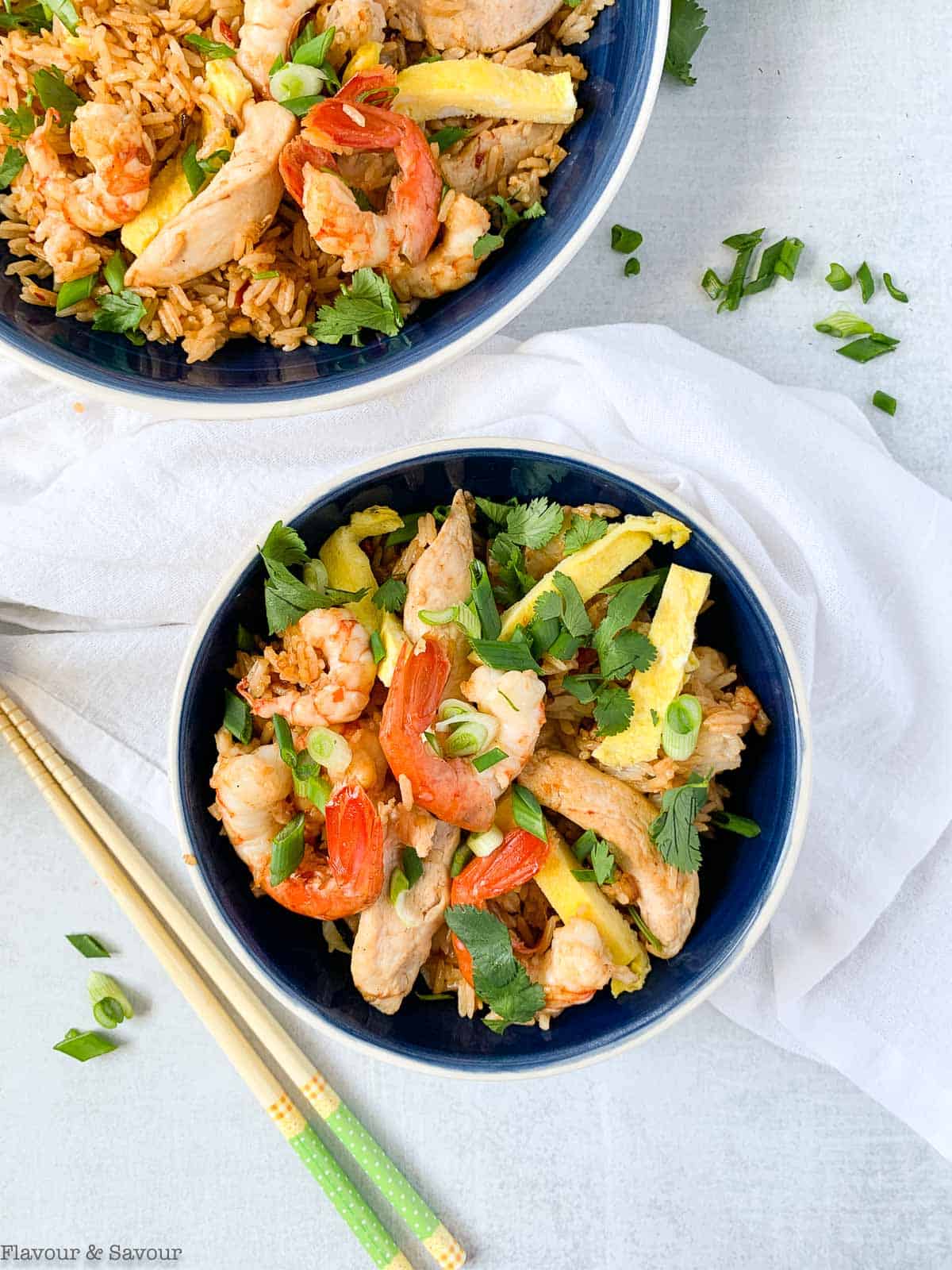 Overhead view of a serving bowl and an individual bowl both filled with Nasi Goreng with chopsticks on the table.