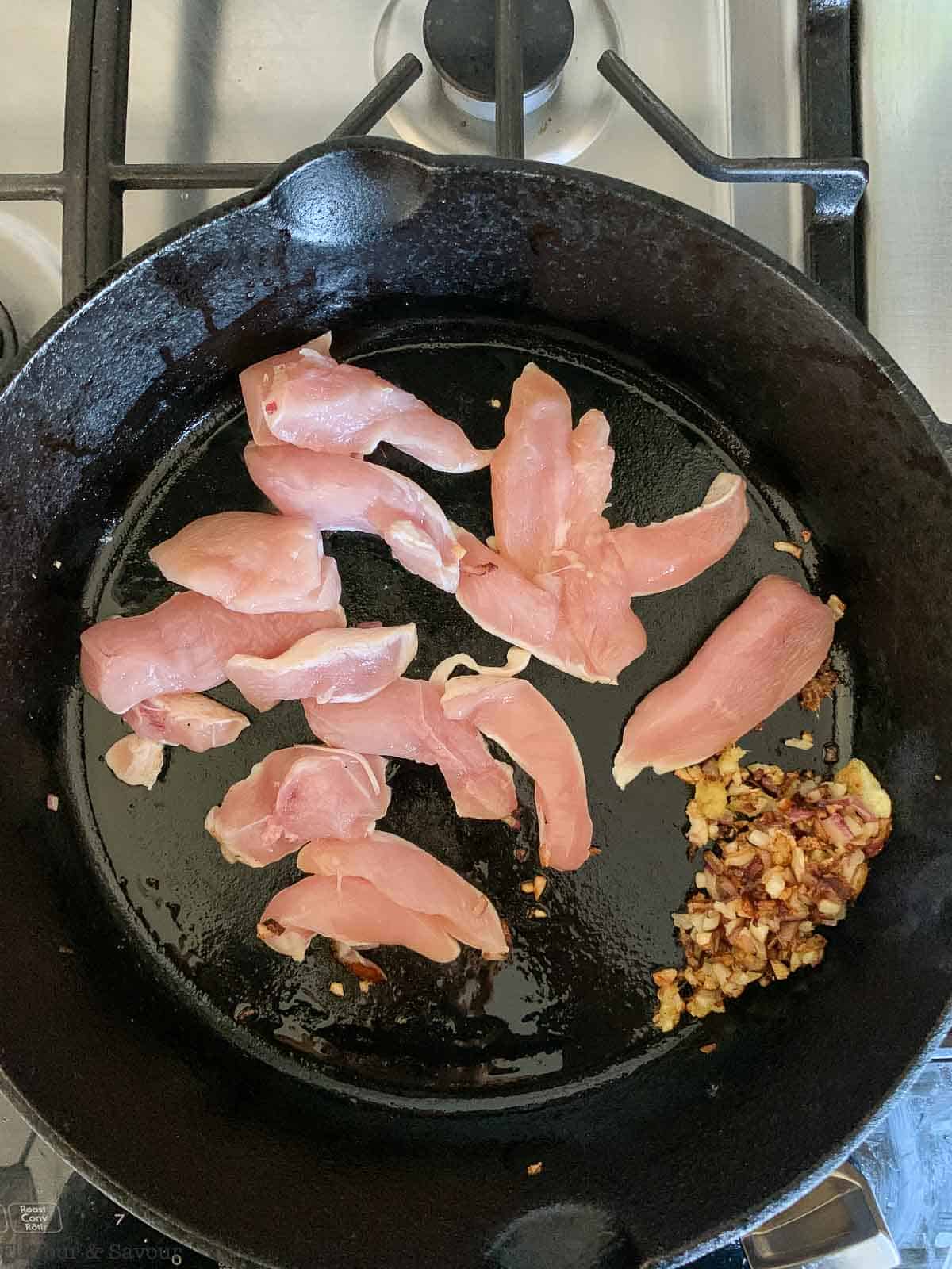 Browning chicken strips in a cast iron pan.