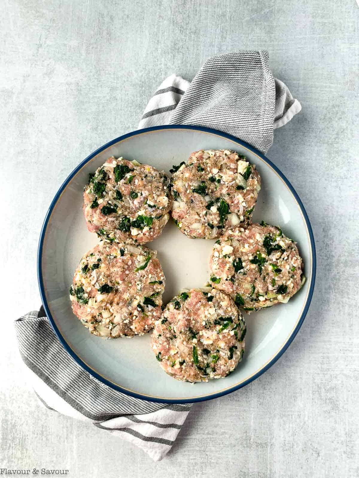 Five uncooked Greek Chicken Burger patties on a plate.