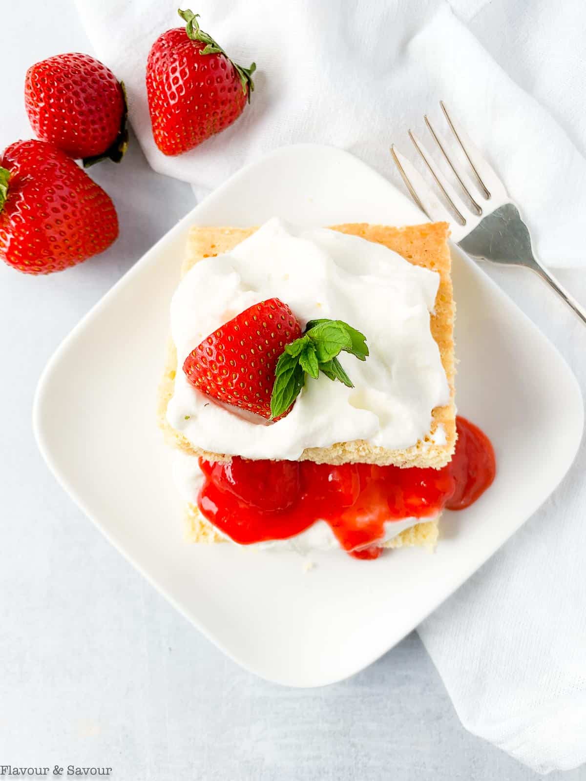 Close up overhead view of a serving of Keto Strawberry Shortcake topped with a fresh strawberry and mint leaves.