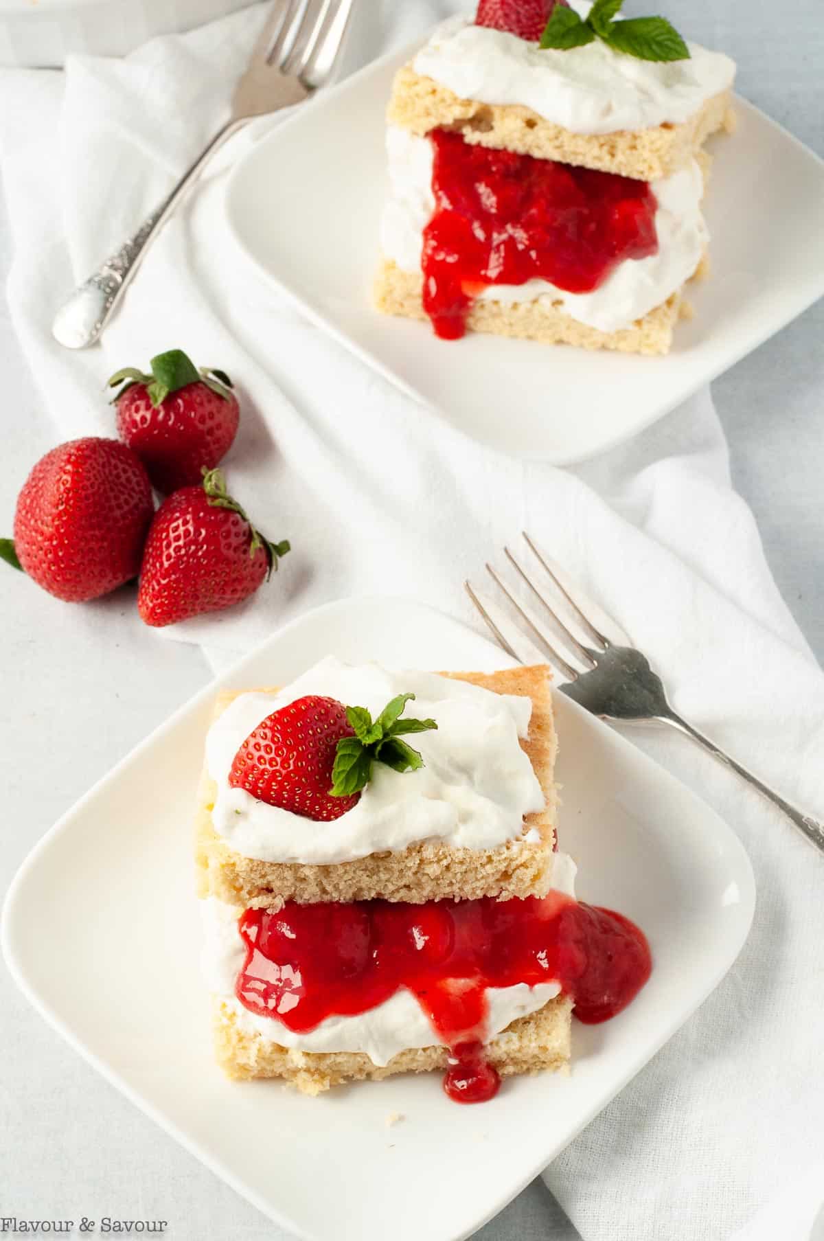 Two servings of Keto Strawberry Shortcake topped with whipped cream, fresh strawberries and a mint leaf.