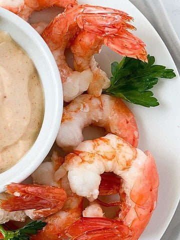 Air fryer lemon garlic shrimp on a plate with a bowl of dip.