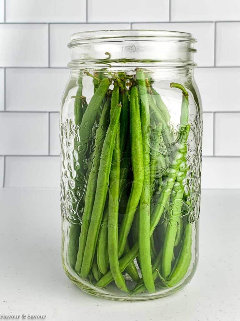 Adding raw green beans to a Mason jar to measure their length.