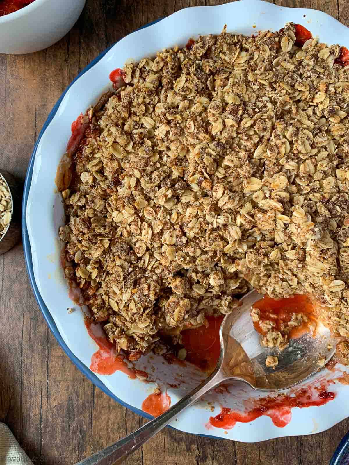 Baked strawberry rhubarb crisp in a baking dish with a spoon.