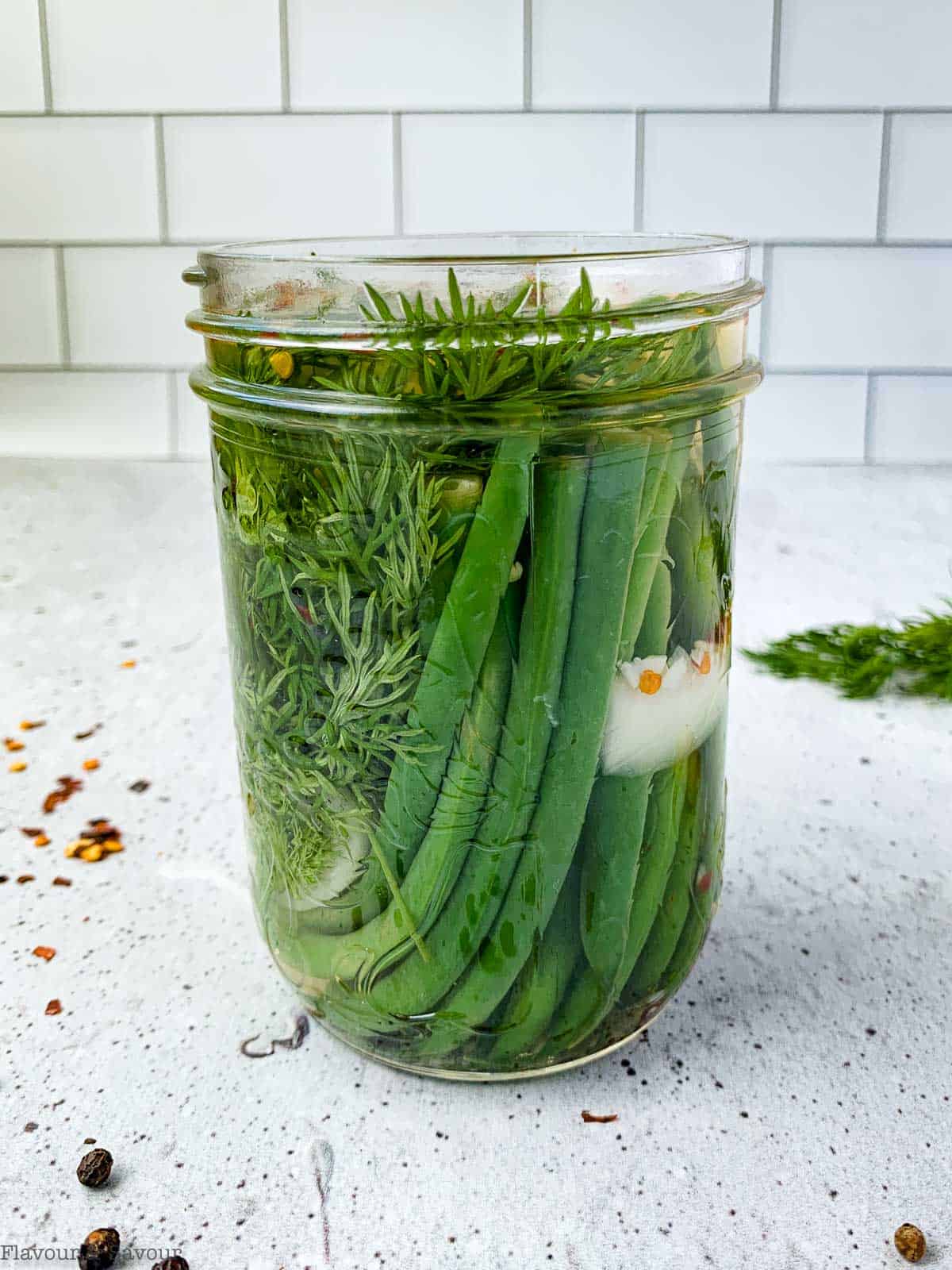 Ajar of refrigerator pickled green beans on a countertop.