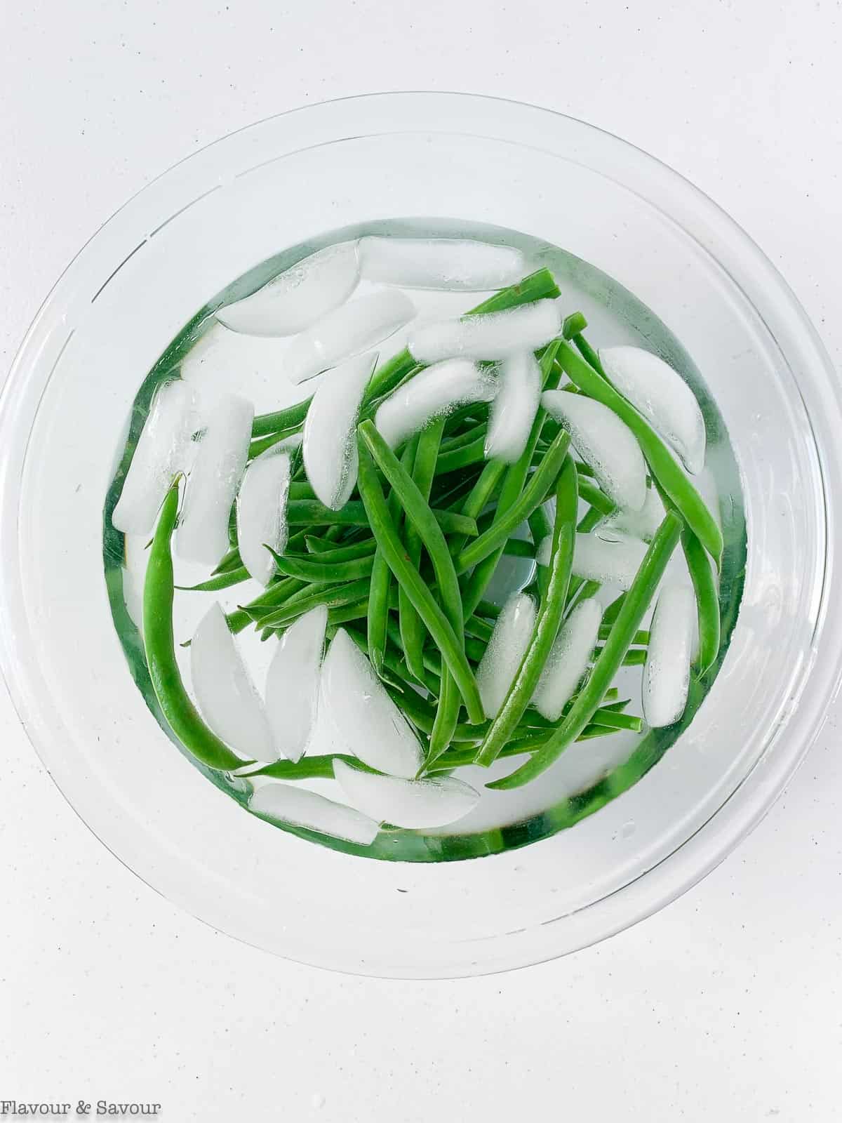 Green beans cooling in an ice bath in a glass bowl.