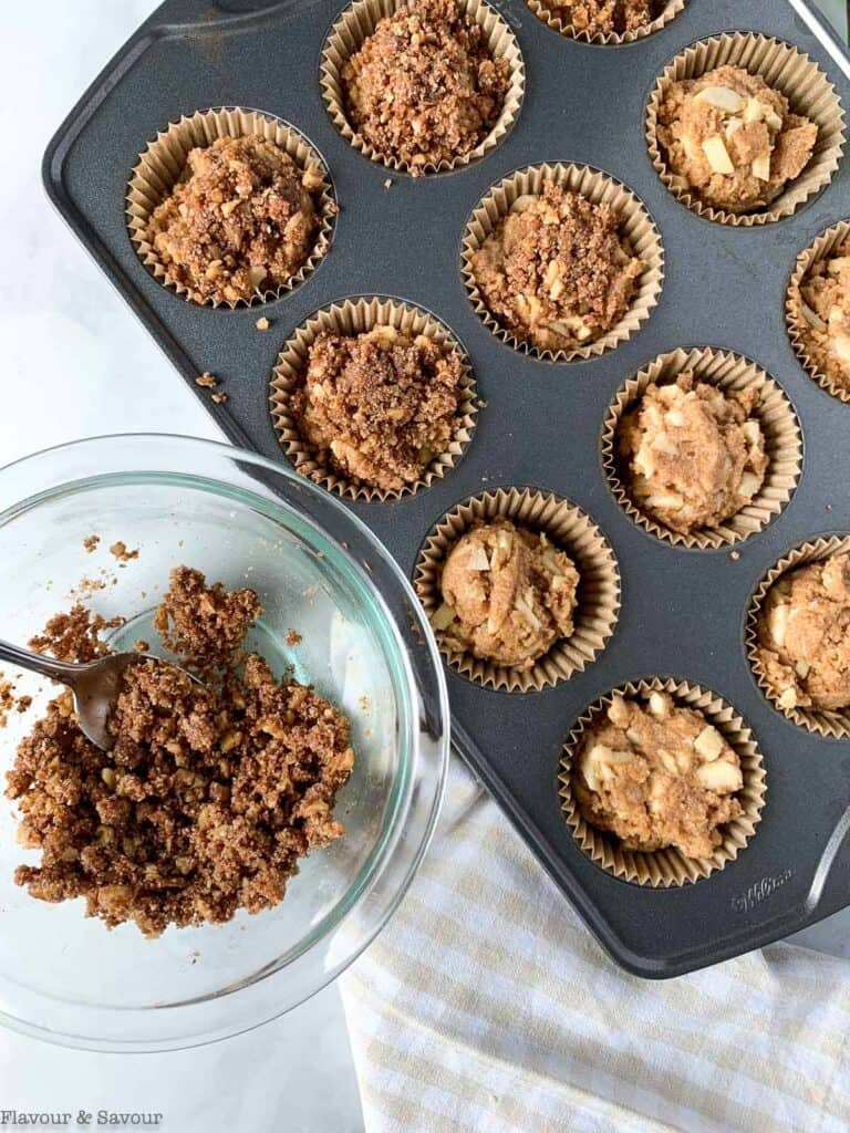 Adding streusel topping to apple muffins in muffin tin liners.