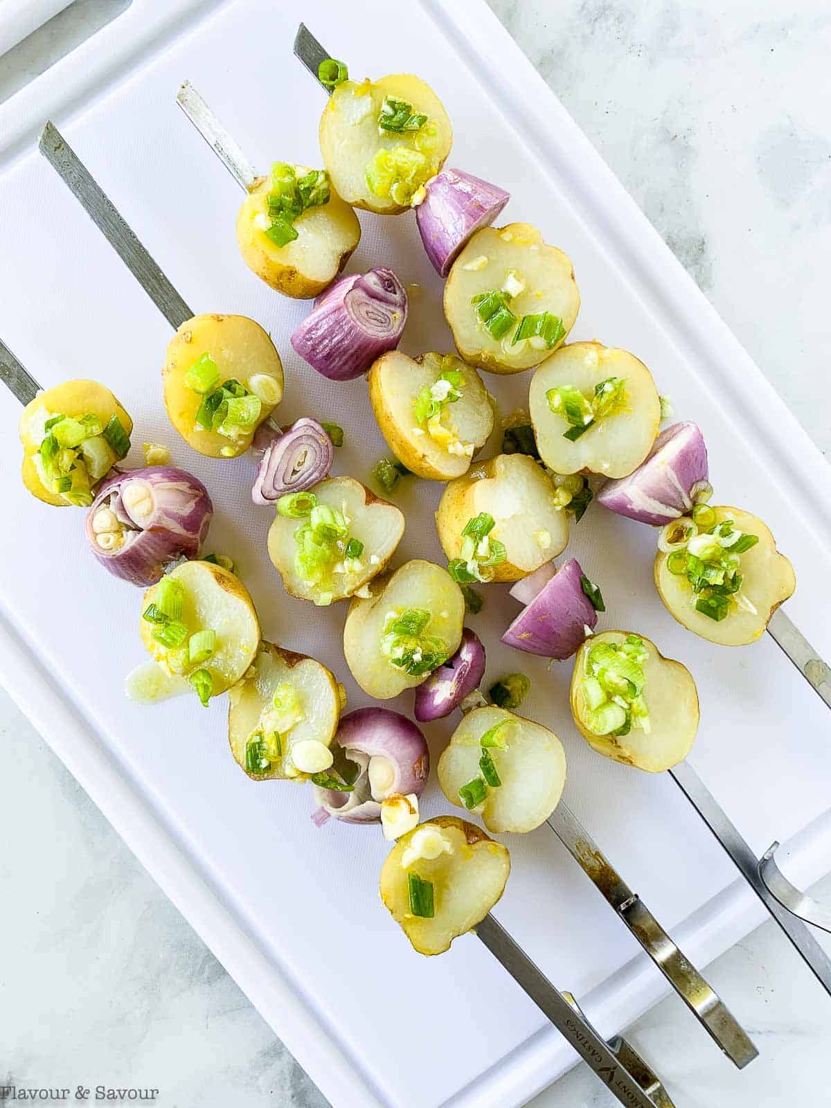 Potatoes and shallots on metal skewers.