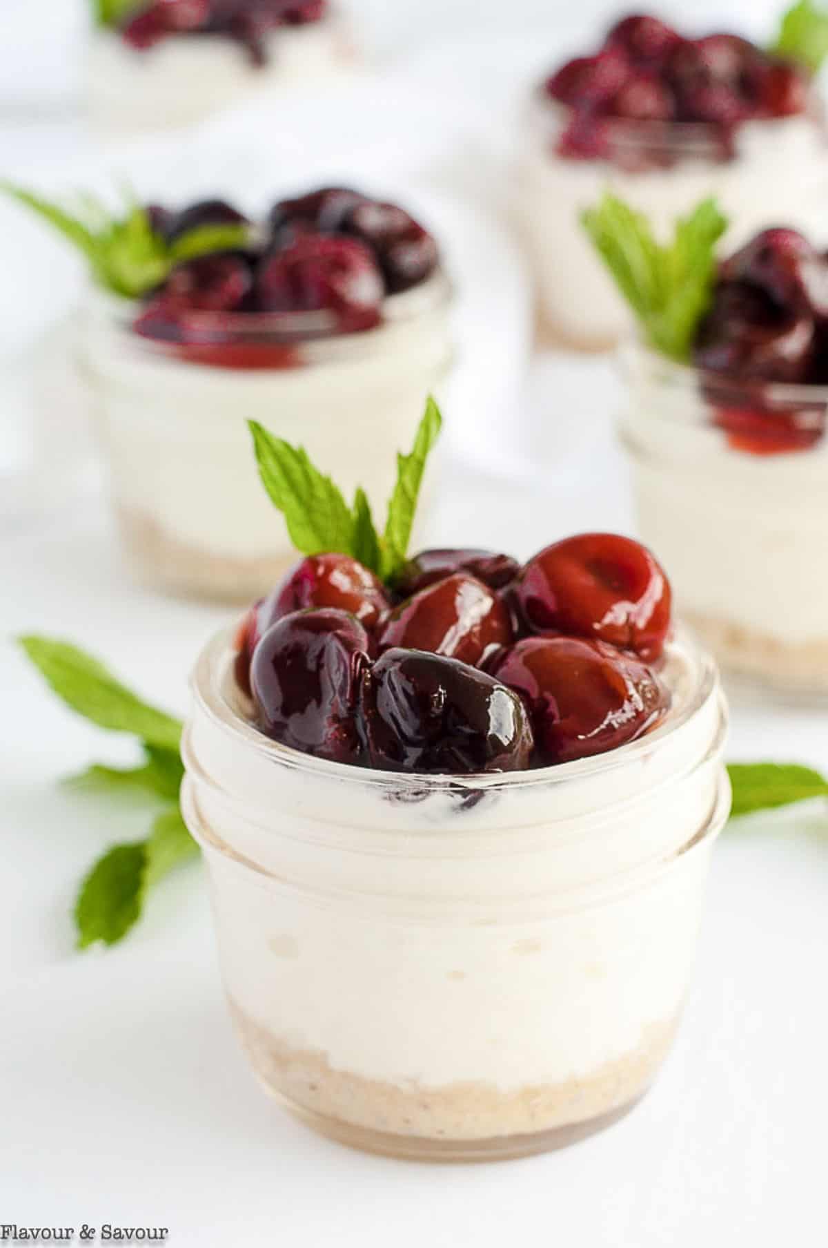 A group of mini no-bake cherry almond cheesecakes in small jars.