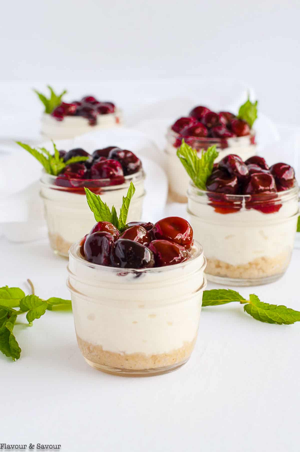 Mini no-bake cherry cheesecake desserts in small mason jars.
