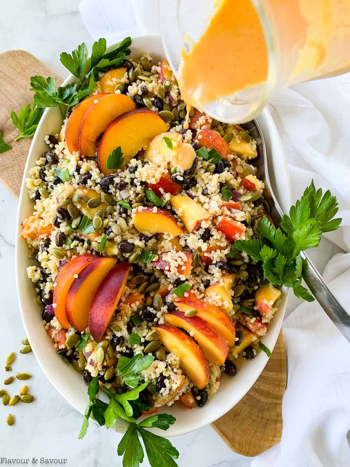 Adding dressing to an oval bowl of quinoa black bean salad with peaches.