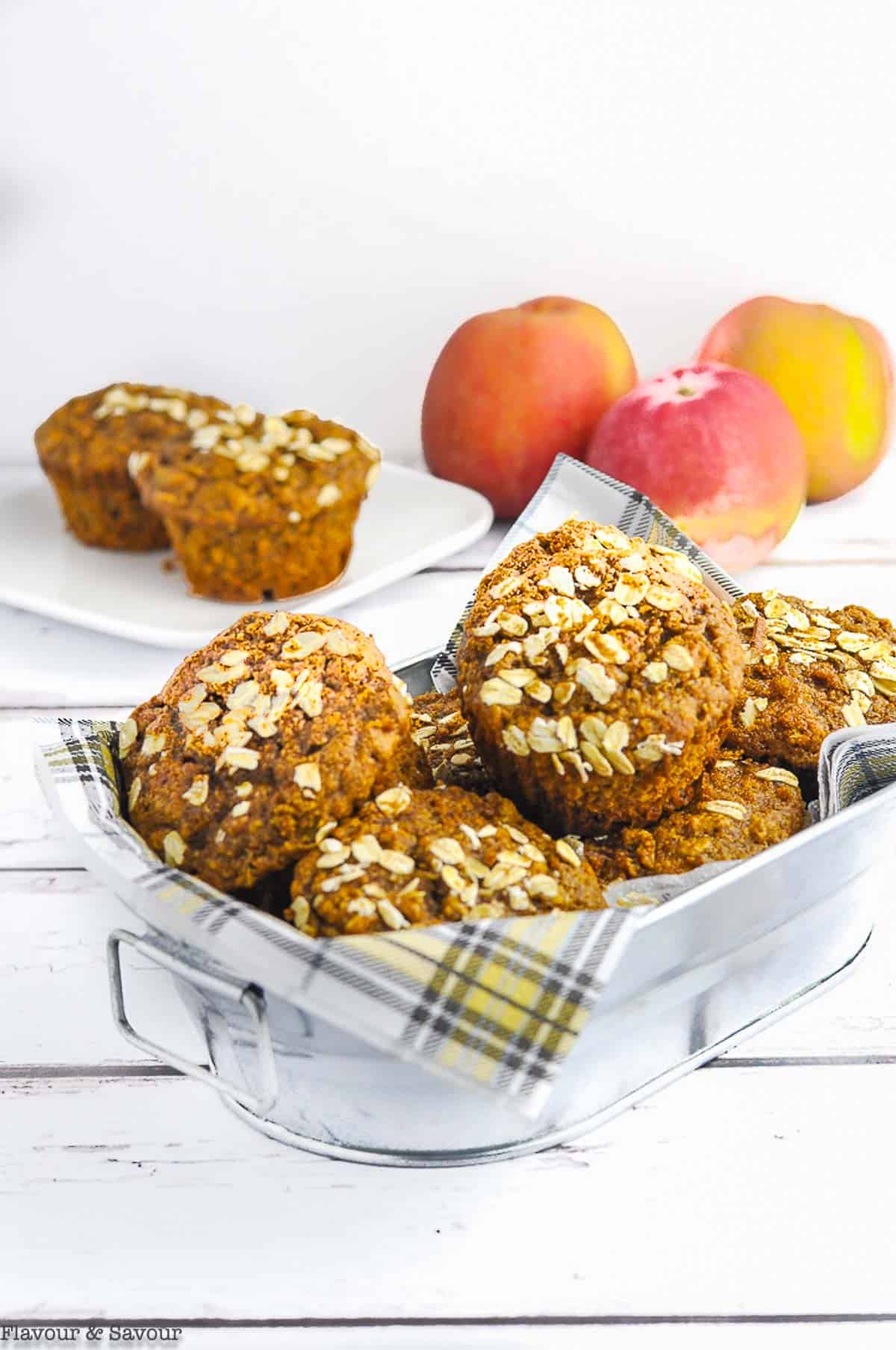 A basket of Gluten-free Apple Oatmeal Muffins with fresh apples in the background.
