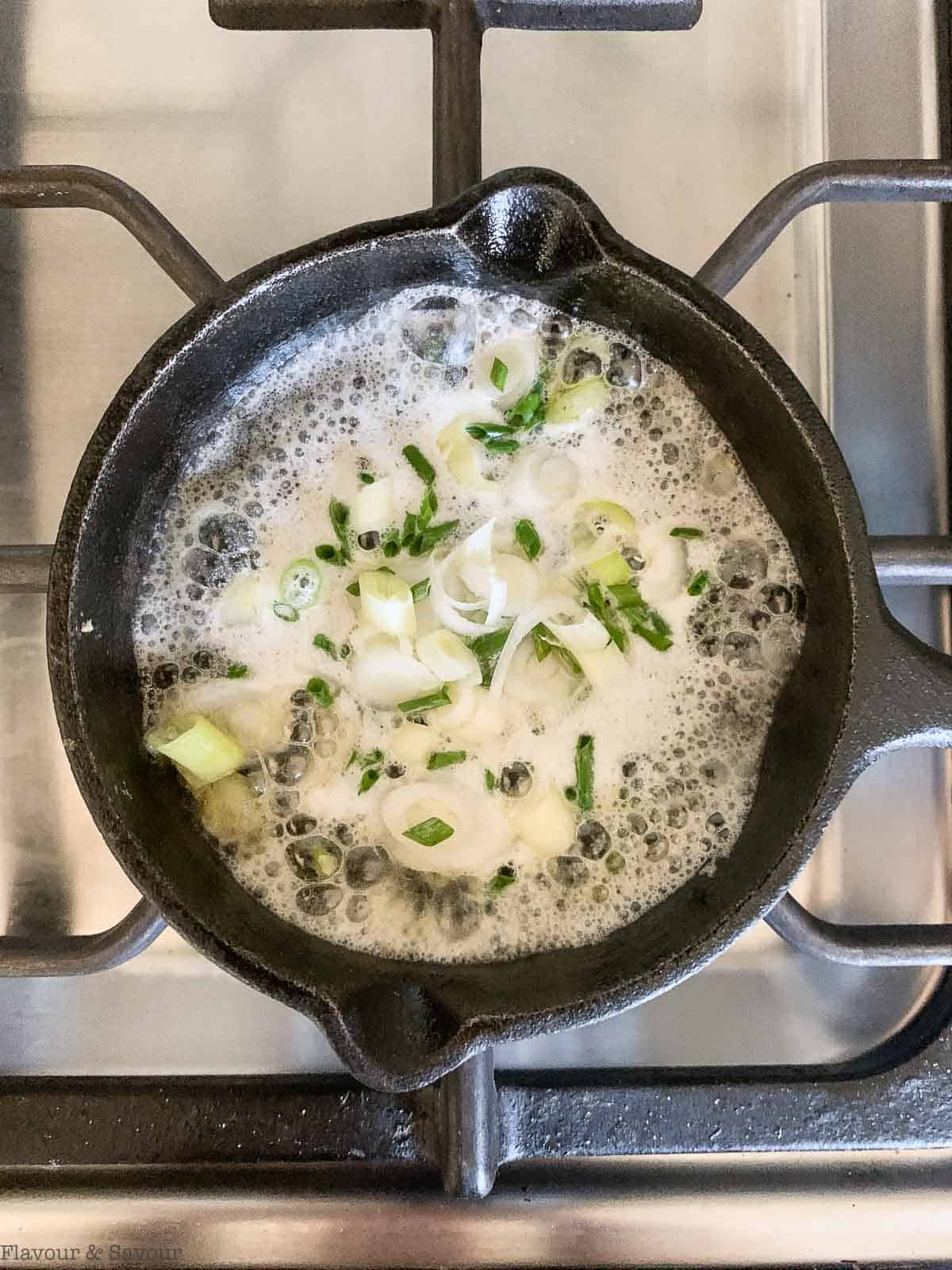 a skillet with melted butter and green onions