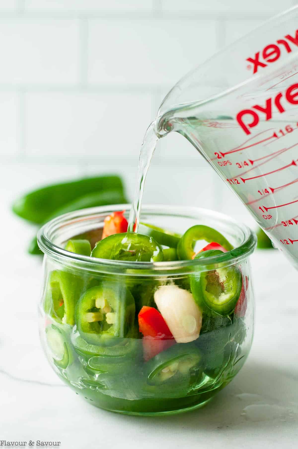 pouring brine on jalapeño pepper slices in a Weck jar