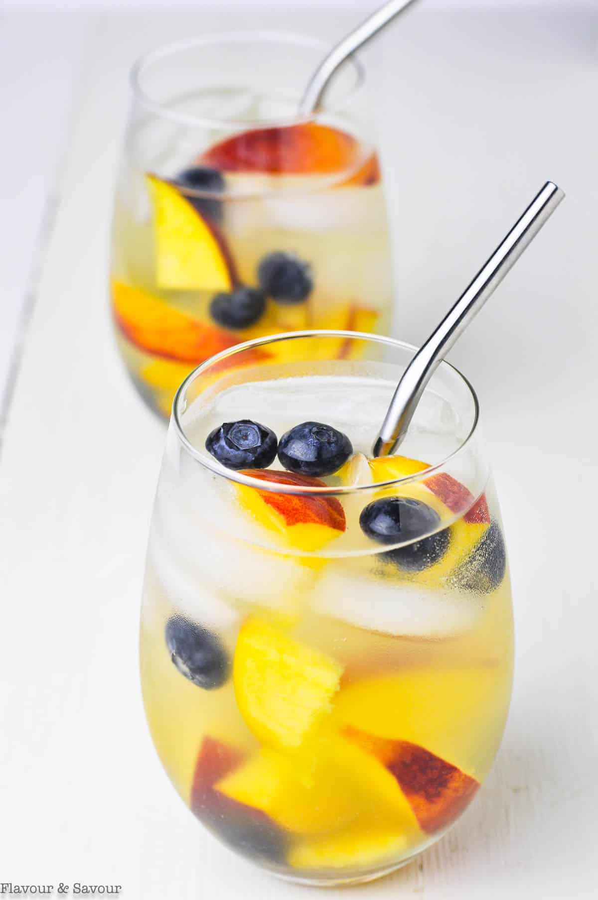 Two glasses of white wine peach sangria with blueberries.