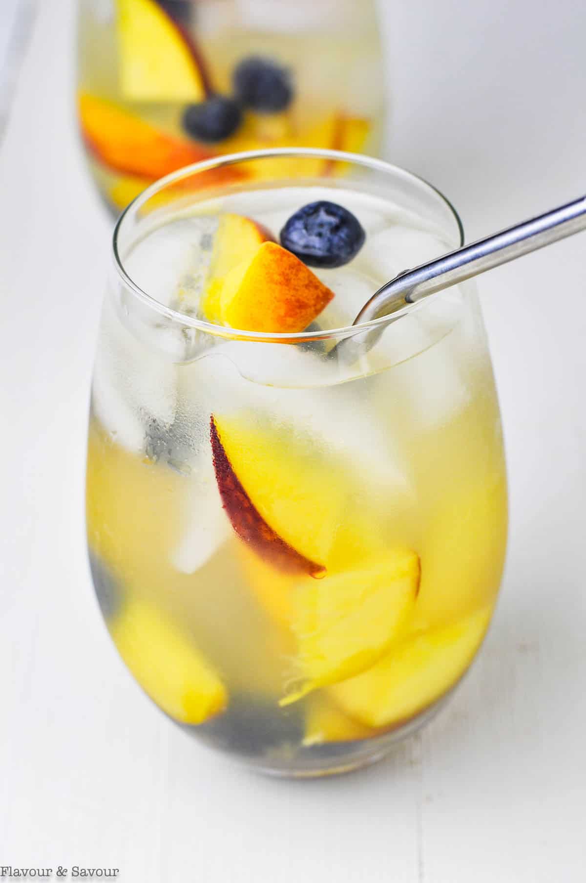 Close up view of a glass of peach sangria with a straw.