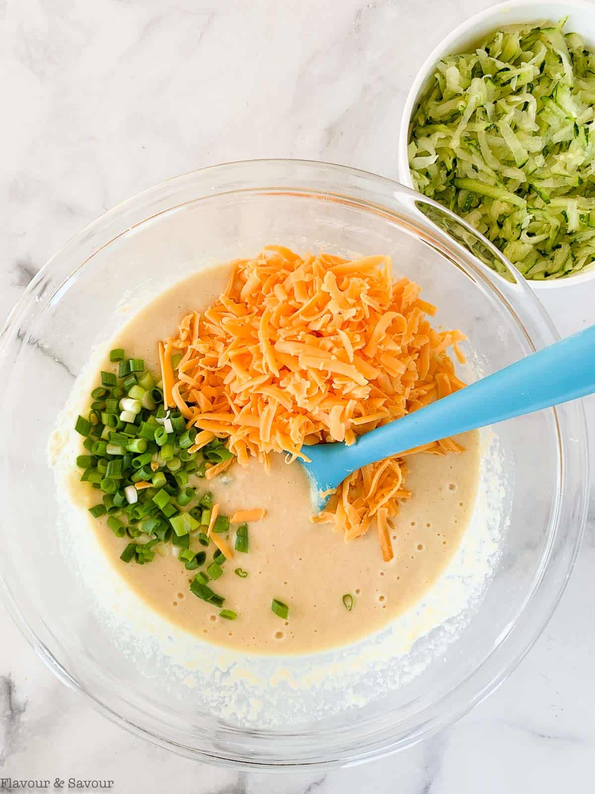 Adding onions and grated cheese to zucchini cheddar muffin batter.