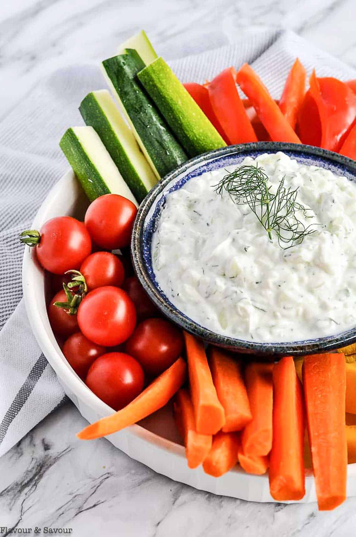 a bowl of Greek Tzatziki Sauce surrounded by raw vegetables