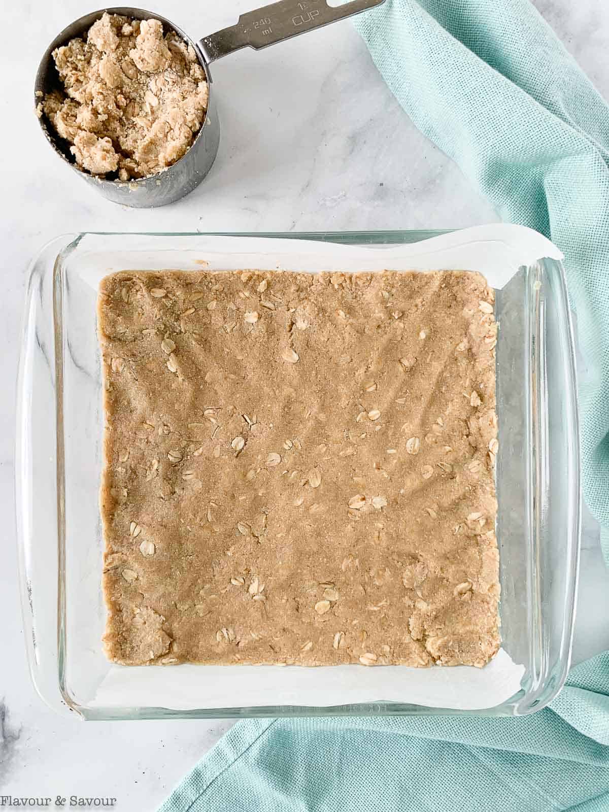 Pressing shortbread crust ingredients into a glass baking dish.