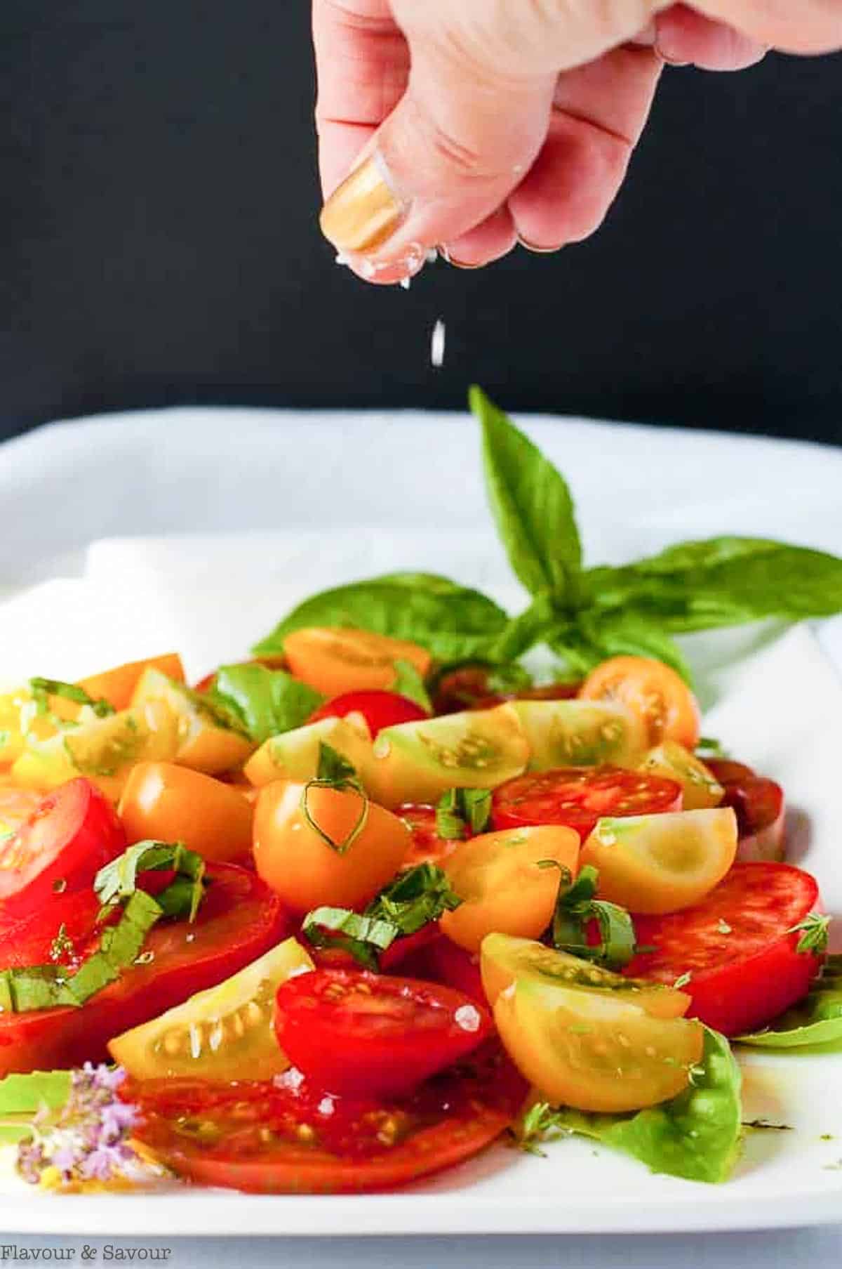 sprinkling coarse salt on Heirloom Tomato Salad with Feta Cheese