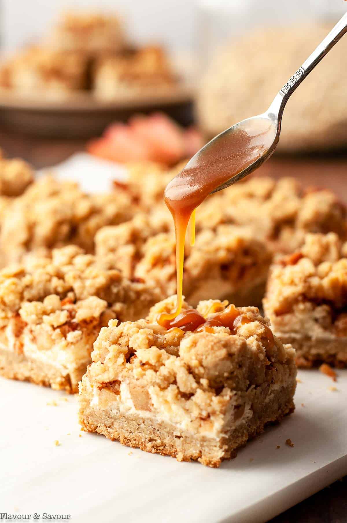 Drizzling caramel sauce from a spoon on Gluten-free Apple Cheesecake Crumble Bars.