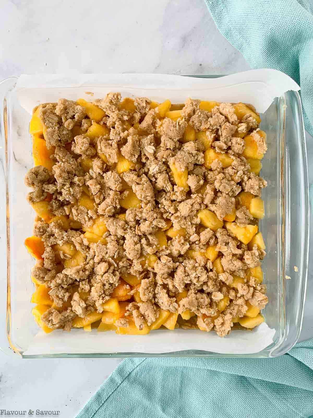 Adding crumb topping to peach crumble bars.