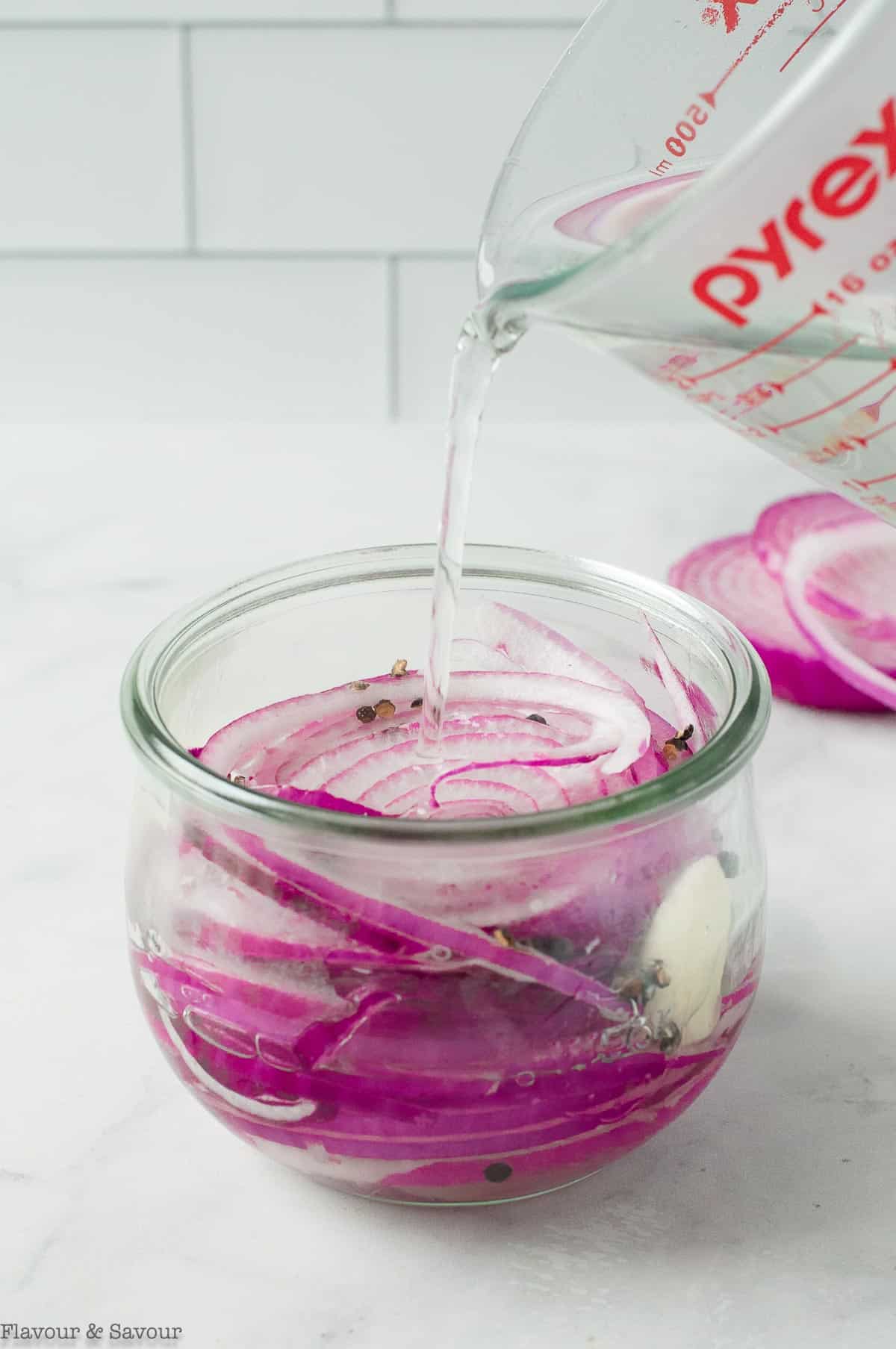 Pouring pickling brine into a jar of sliced red onions.