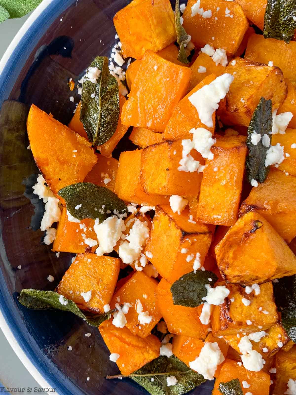 close up view of Butternut squash cubes in a blue bowl with feta cheese and sage leaves