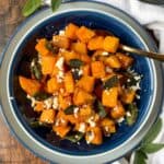 A bowl of cubed butternut squash with feta cheese and sage leaves