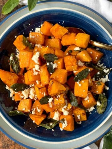 A bowl of cubed butternut squash with feta cheese and sage leaves