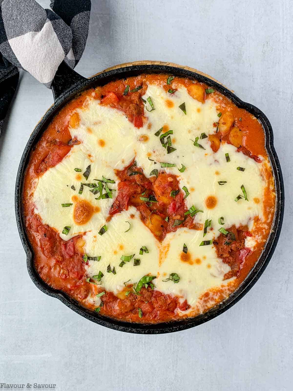 A cast iron skillet with tomato gnocchi bake with plant-based meat and melted cheese.