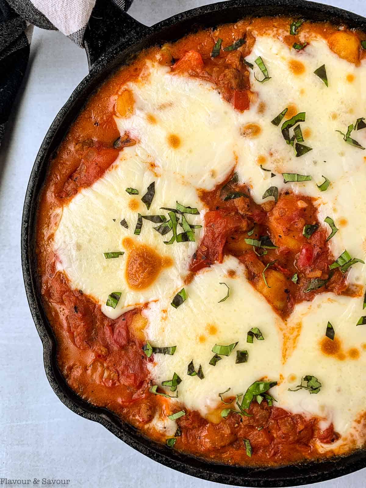 Close up view of a skillet filled with cheesy tomato gnocchi bake