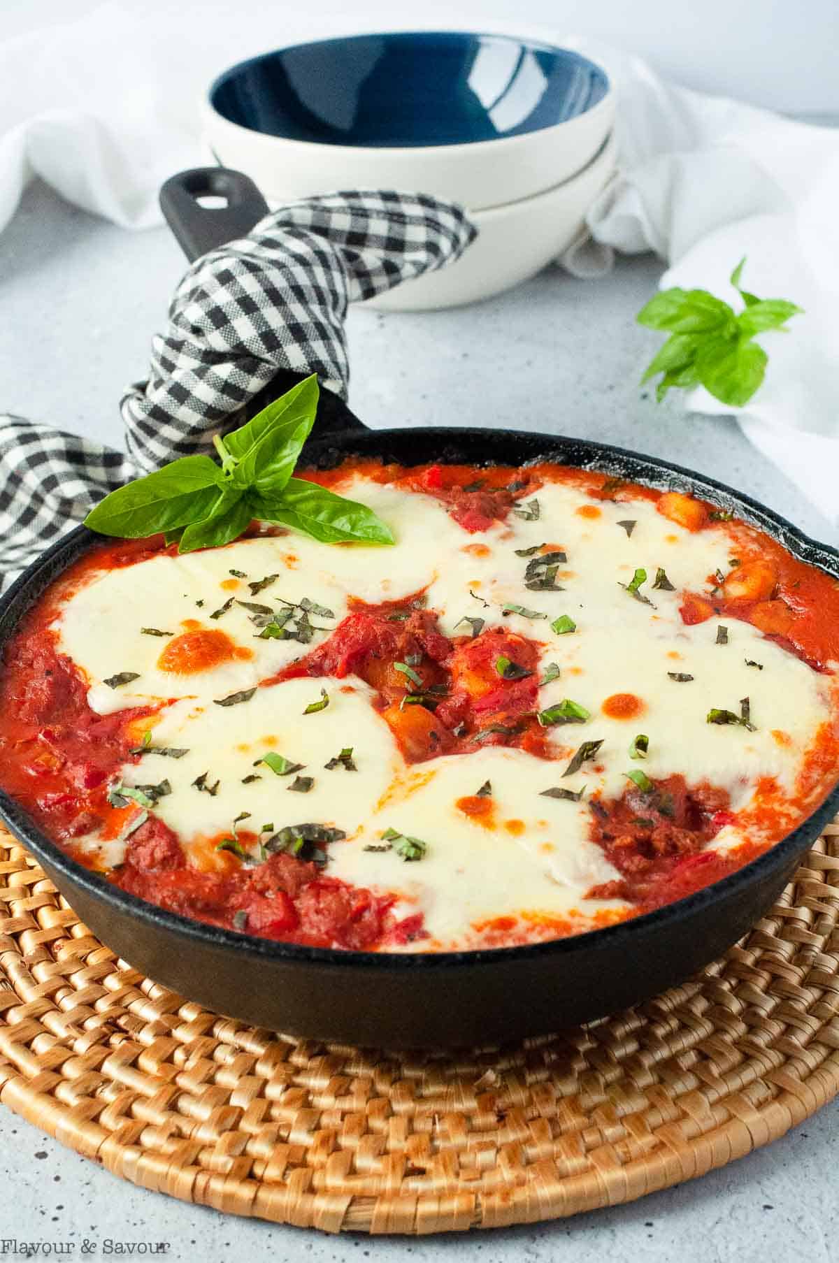 Skillet with baked gnocchi with tomatoes and cheese on a hot pad.