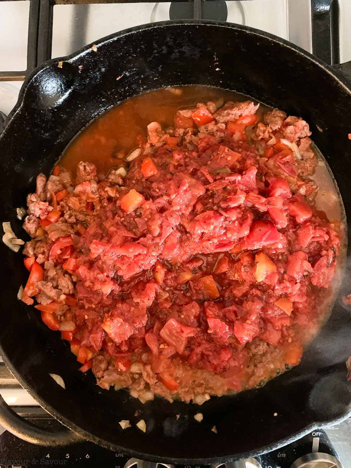 tomatoes added to onions, garlic and plant-based meat in a skillet.