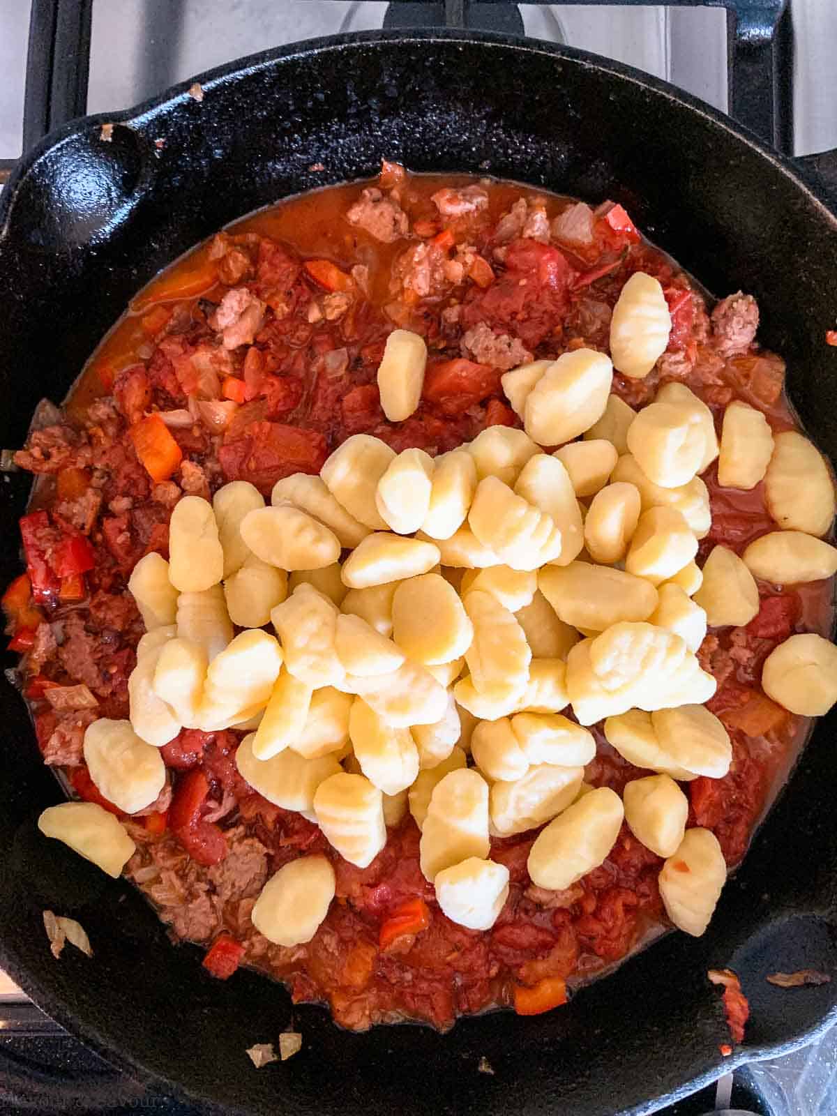 adding gnocchi to tomato and plant-based meat in a cast iron skillet.