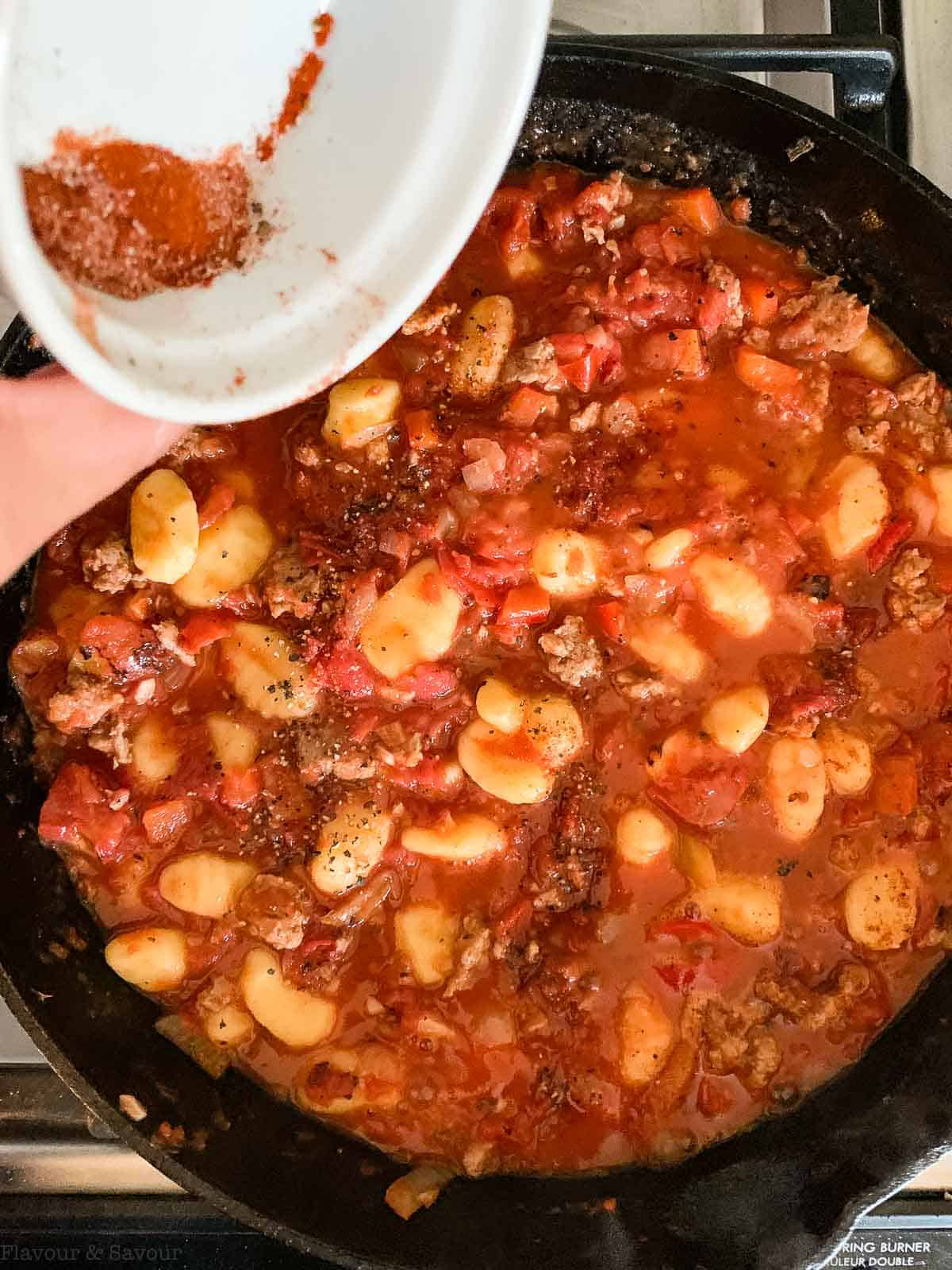 adding seasonings to cheesy tomato gnocchi bake.